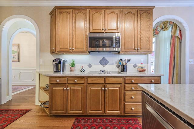 kitchen with stainless steel microwave, black electric stovetop, light wood-type flooring, light stone counters, and wainscoting