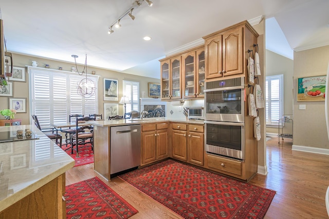 kitchen featuring glass insert cabinets, a toaster, light wood-type flooring, appliances with stainless steel finishes, and a peninsula