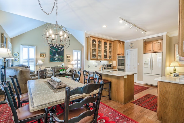 dining room with a notable chandelier, light wood-style flooring, ornamental molding, a toaster, and vaulted ceiling