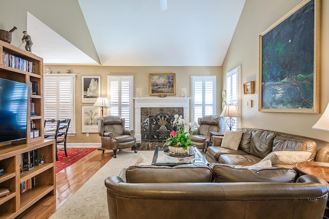 living room featuring a premium fireplace, baseboards, lofted ceiling, and wood finished floors