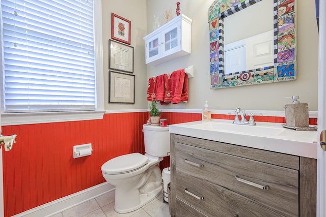 half bathroom featuring tile patterned flooring, wooden walls, toilet, wainscoting, and vanity