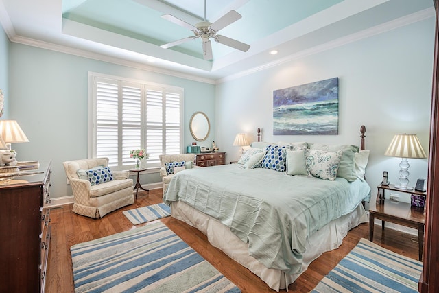 bedroom featuring a ceiling fan, wood finished floors, baseboards, a tray ceiling, and ornamental molding