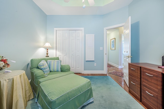 bedroom with a raised ceiling, a ceiling fan, wood finished floors, a closet, and baseboards