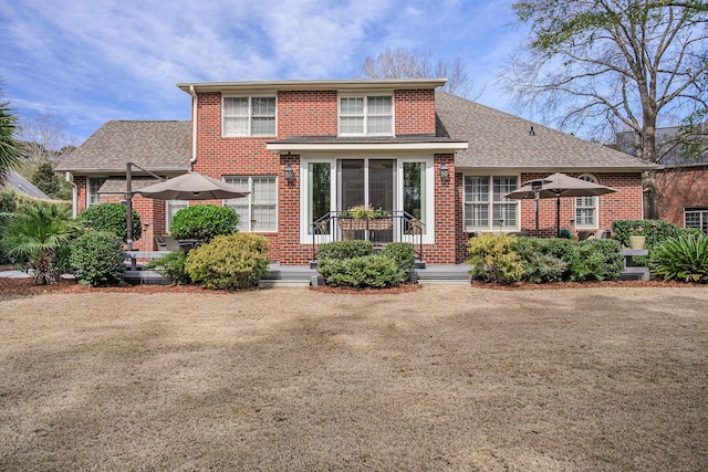 traditional home featuring brick siding, a shingled roof, and a front yard