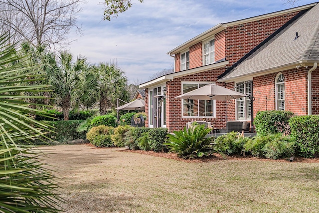 view of property exterior with brick siding, a lawn, and roof with shingles