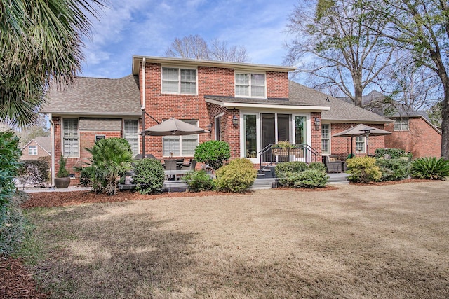 rear view of property featuring brick siding, a lawn, and a shingled roof