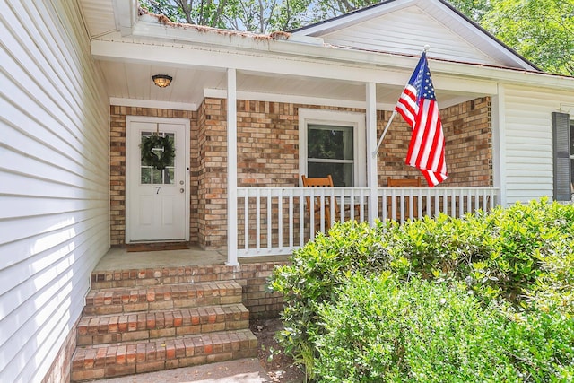 entrance to property featuring a porch and brick siding