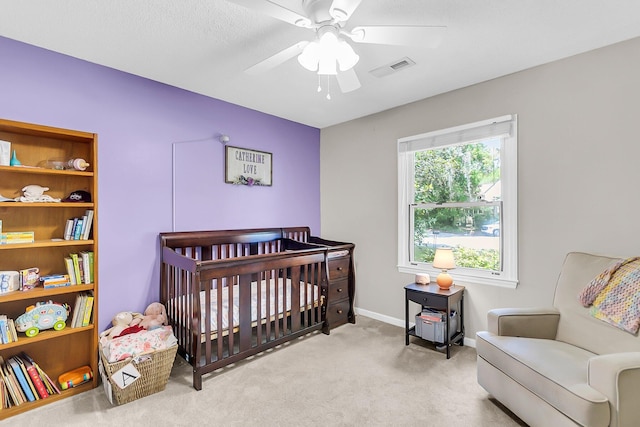 bedroom with a nursery area, visible vents, carpet floors, a ceiling fan, and baseboards