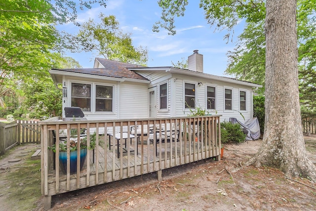 rear view of house featuring a chimney, a wooden deck, a shingled roof, and fence