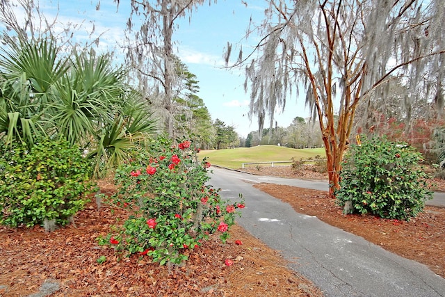 surrounding community with golf course view, a lawn, and aphalt driveway