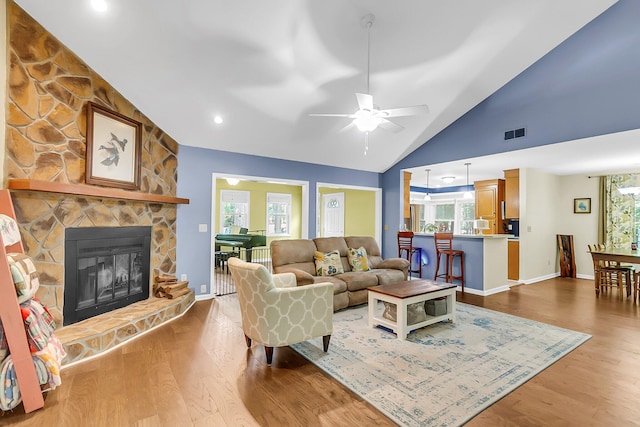 living room with vaulted ceiling, a fireplace, visible vents, and wood finished floors