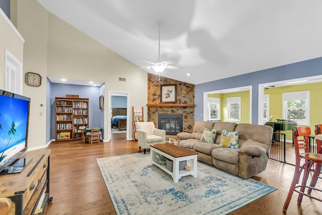 living area with wood finished floors, a ceiling fan, a stone fireplace, and high vaulted ceiling