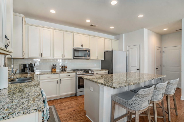 kitchen with light stone counters, appliances with stainless steel finishes, dark hardwood / wood-style floors, and a center island