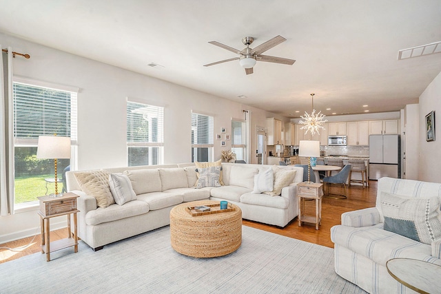 living room with plenty of natural light, ceiling fan with notable chandelier, and light hardwood / wood-style flooring