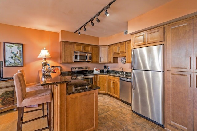 330 Concord St Unit 8E, Charleston, SC 29401 - kitchen with appliances with stainless steel finishes, a kitchen bar, brown cabinetry, dark stone countertops, and track lighting