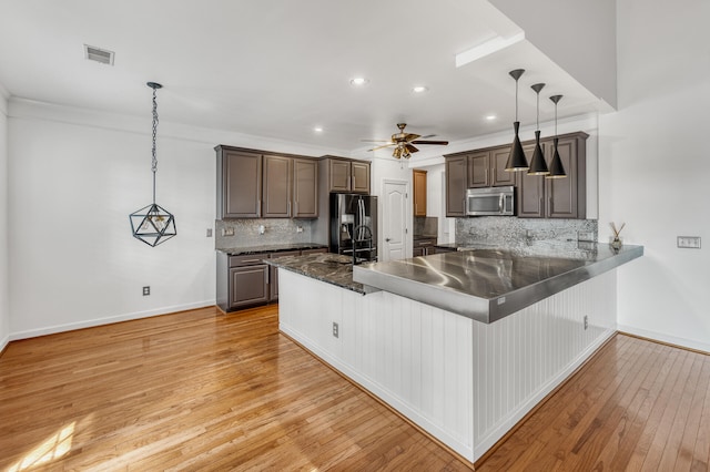 kitchen featuring decorative light fixtures, appliances with stainless steel finishes, light wood-type flooring, and kitchen peninsula