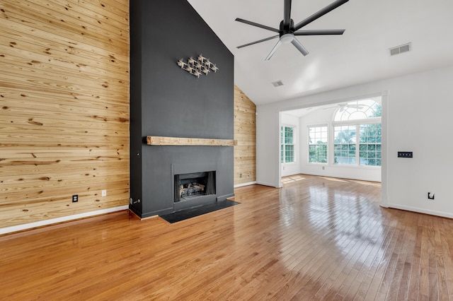 unfurnished living room with ceiling fan, wooden walls, high vaulted ceiling, hardwood / wood-style flooring, and a fireplace