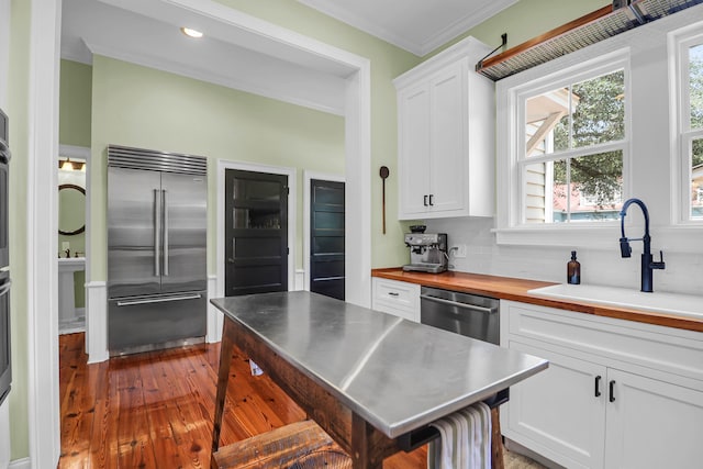 kitchen featuring appliances with stainless steel finishes, sink, white cabinets, hardwood / wood-style flooring, and decorative backsplash