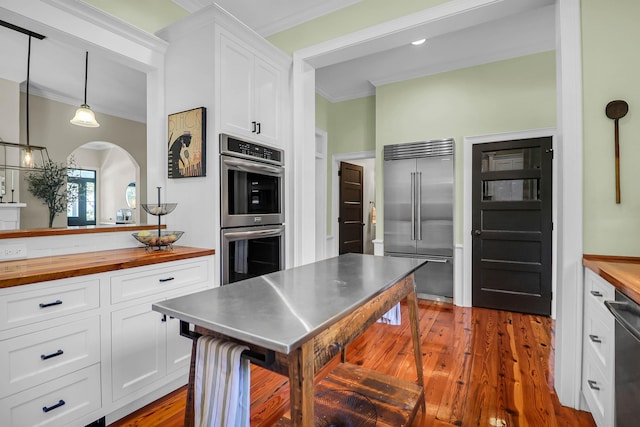 kitchen with dark hardwood / wood-style floors, white cabinetry, wooden counters, ornamental molding, and stainless steel appliances