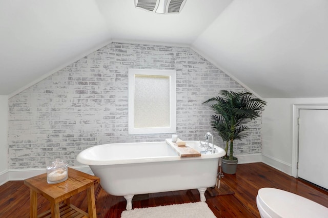 bathroom featuring a bathing tub, vaulted ceiling, brick wall, and toilet