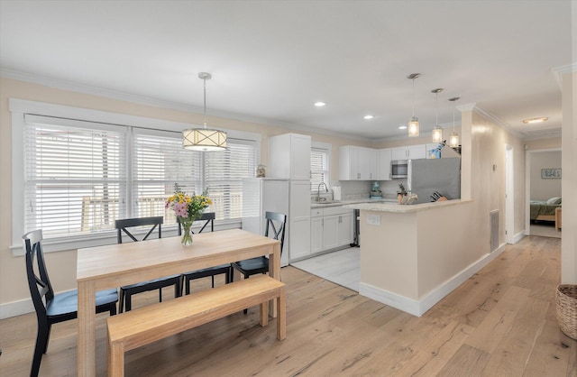 kitchen with a sink, appliances with stainless steel finishes, ornamental molding, a peninsula, and baseboards
