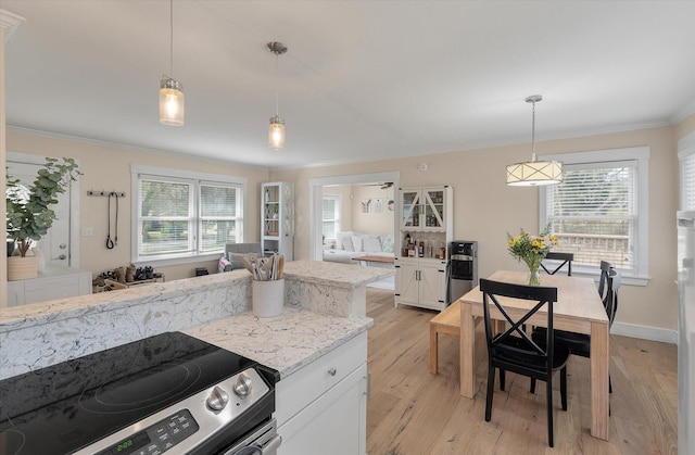 kitchen featuring stainless steel range with electric stovetop, white cabinets, crown molding, light stone countertops, and healthy amount of natural light