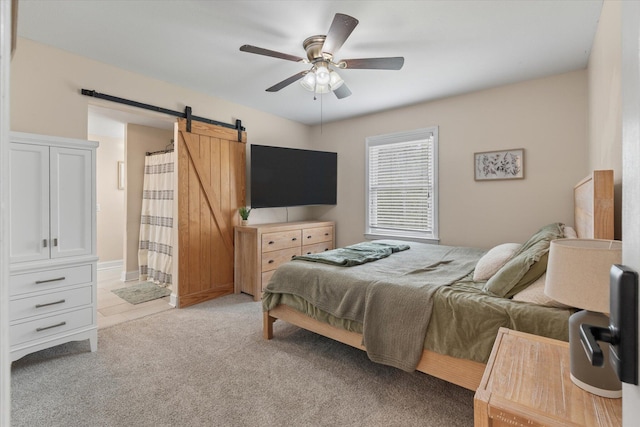 bedroom featuring a barn door, light colored carpet, ceiling fan, and connected bathroom