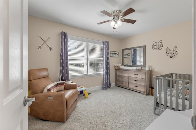 bedroom featuring light carpet, a crib, baseboards, and a ceiling fan