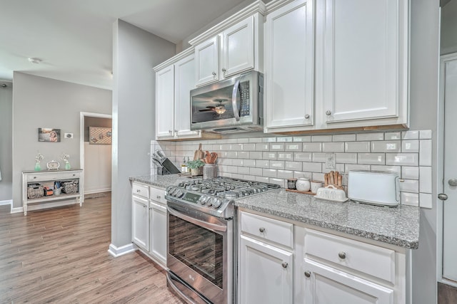 kitchen with light stone counters, white cabinetry, appliances with stainless steel finishes, backsplash, and light wood finished floors