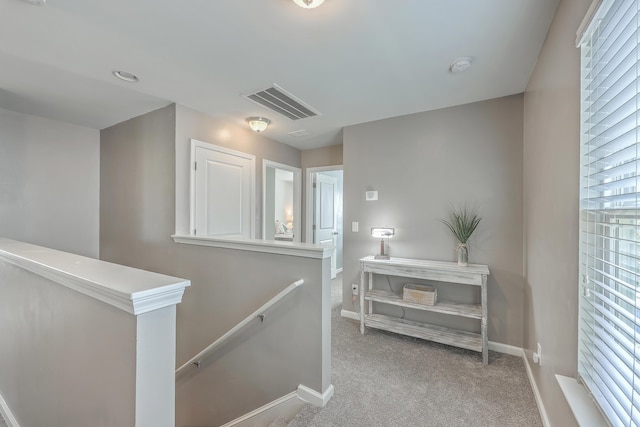 hallway featuring carpet, visible vents, baseboards, and an upstairs landing