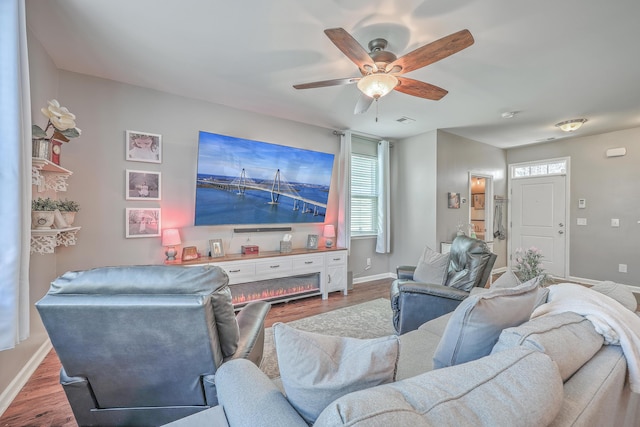 living room featuring ceiling fan, visible vents, baseboards, and wood finished floors