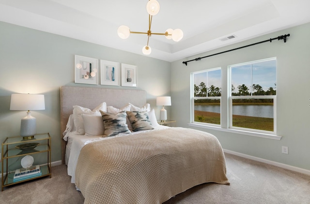 carpeted bedroom with an inviting chandelier and a tray ceiling