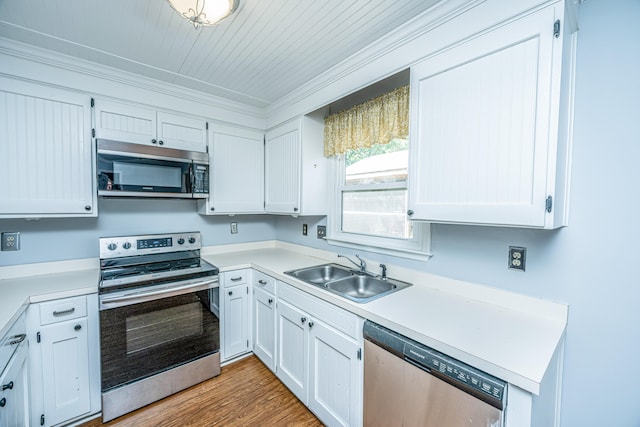 kitchen with appliances with stainless steel finishes, sink, light wood-type flooring, white cabinetry, and ornamental molding