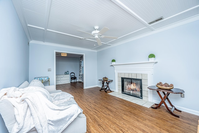 living room with ceiling fan, a tiled fireplace, crown molding, and hardwood / wood-style floors