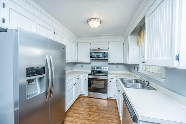 kitchen featuring appliances with stainless steel finishes, sink, white cabinets, crown molding, and hardwood / wood-style flooring