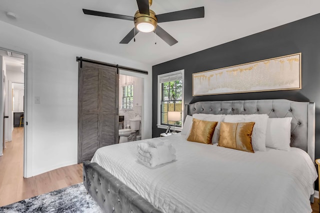 bedroom with wood finished floors, a barn door, ensuite bath, and a ceiling fan