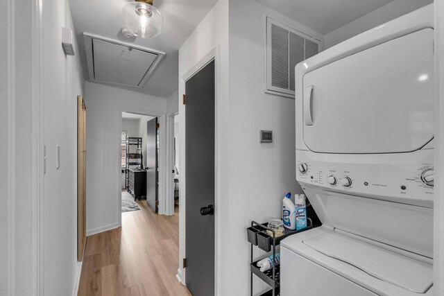 laundry room with stacked washer and clothes dryer, attic access, and light wood-style flooring
