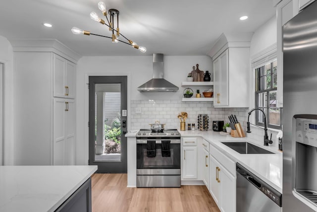 kitchen with stainless steel appliances, wall chimney range hood, a sink, decorative backsplash, and light wood-style floors