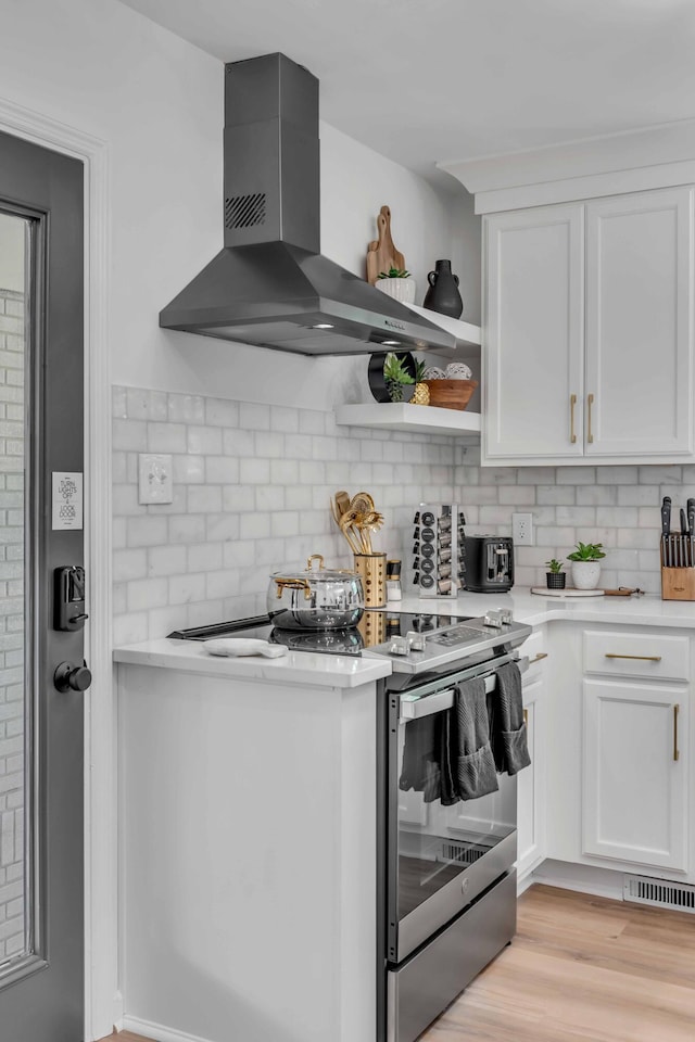 kitchen featuring wall chimney range hood, stainless steel electric range, and white cabinetry