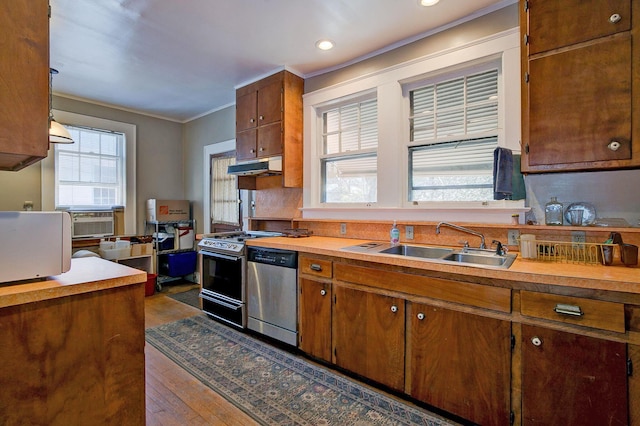 kitchen featuring crown molding, under cabinet range hood, gas range oven, stainless steel dishwasher, and a sink