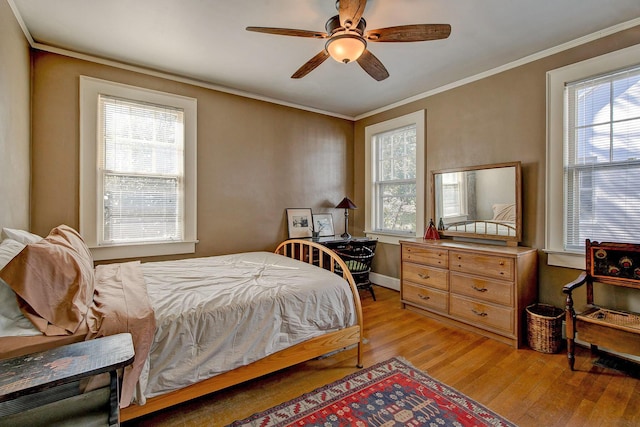 bedroom with a ceiling fan, multiple windows, light wood-style floors, and ornamental molding