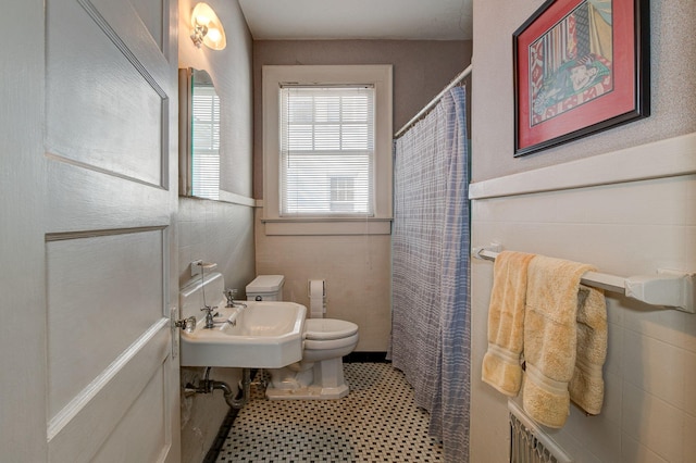 bathroom with a sink, a shower with shower curtain, toilet, and tile walls