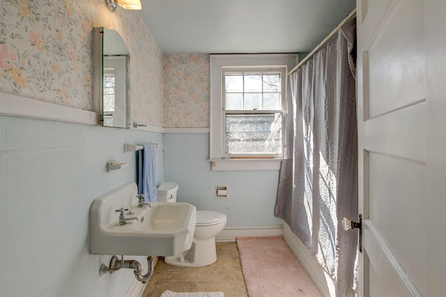 bathroom with wainscoting, wallpapered walls, toilet, and a sink