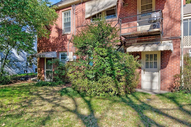 exterior space featuring a balcony, a yard, and brick siding