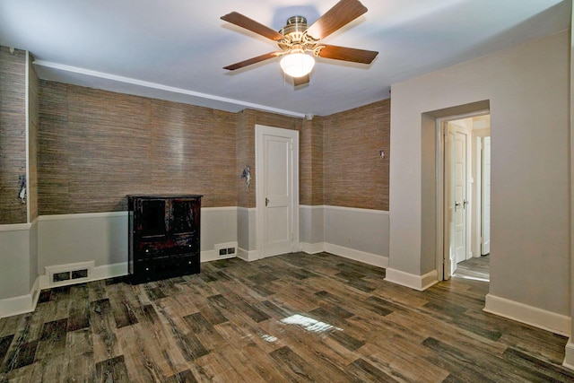 empty room with ceiling fan, visible vents, wood finished floors, and wainscoting