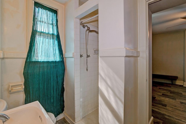 bathroom with a tile shower, a sink, toilet, and wood finished floors