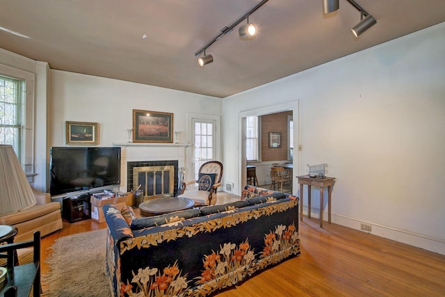 living room featuring track lighting, a tile fireplace, baseboards, and wood finished floors