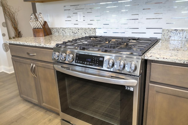 409 Pine Lake Ct, Manning, SC 29102 - kitchen featuring stainless steel gas stove, light wood-type flooring, tasteful backsplash, and light stone counters