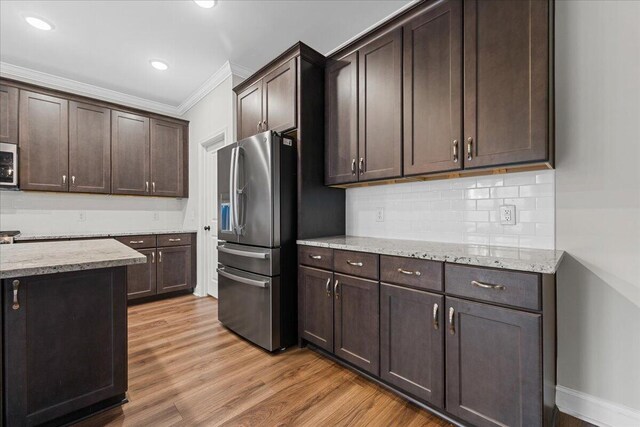 kitchen featuring dark brown cabinetry, stainless steel appliances, light stone counters, light hardwood / wood-style flooring, and ornamental molding