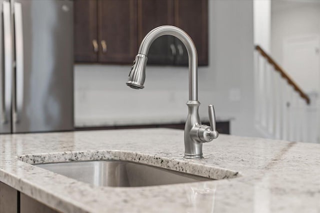 details featuring dark brown cabinetry, light stone counters, and sink